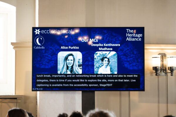 TV screen showing The Heritage Alliance information and live subtitles by Stagetext