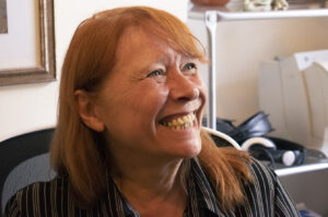 A red haired woman sits at her desk smiling broadly