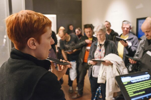 A photo of a Wellcome Collection tour with visitors holding tablets with live subtitles on them.